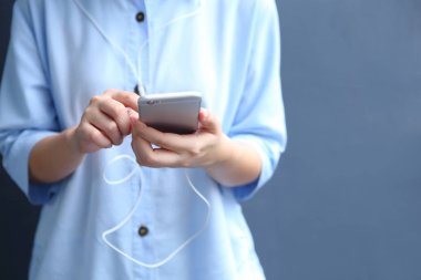 Kadın kulaklık takıyor ve akıllı telefon kullanıyor.