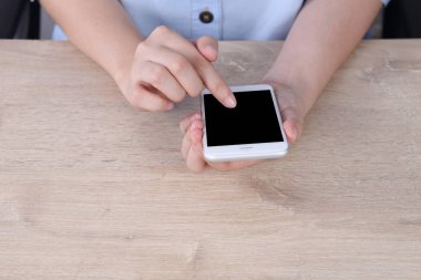 Woman dress blue shirt using and touching mock up smartphone on wooden desk