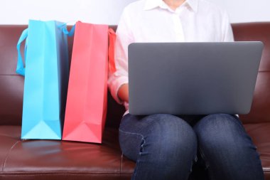 Woman sit on sofa with shooping bag beside and using laptop