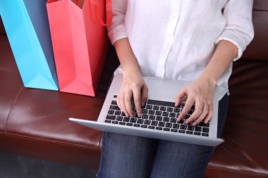 Woman sit on sofa with shooping bag beside and using laptop