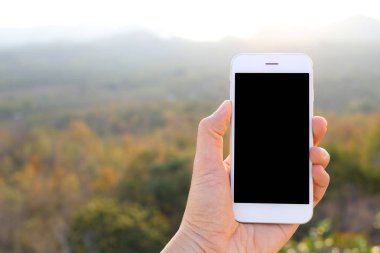 Hand holding mockup smartphone with sunlight and mountains background