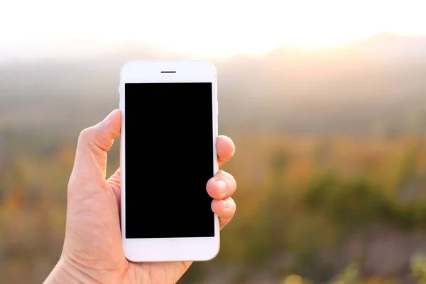Рука держит макет смартфона с солнечным светом и горный backgr — стоковое фото