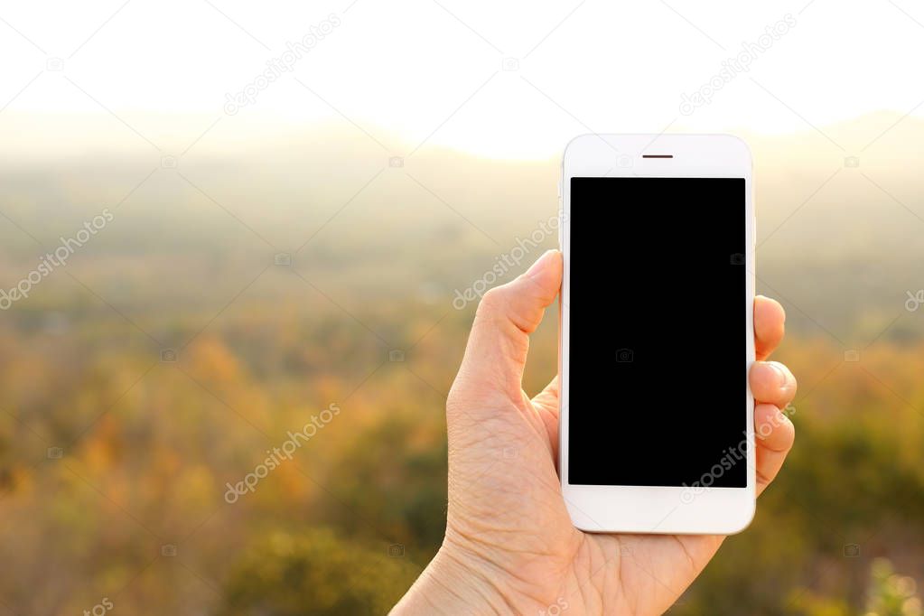 Hand holding mockup smartphone with sunlight and mountain backgr