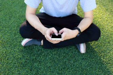Kullanım smartphone yapay çim üzerinde oturan adam