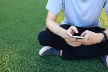 Kullanım smartphone yapay çim üzerinde oturan adam
