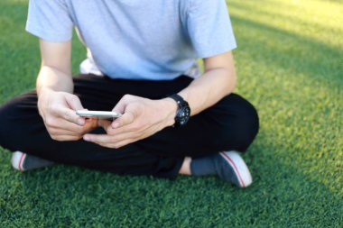 Kullanım smartphone yapay çim üzerinde oturan adam