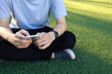 Kullanım smartphone yapay çim üzerinde oturan adam