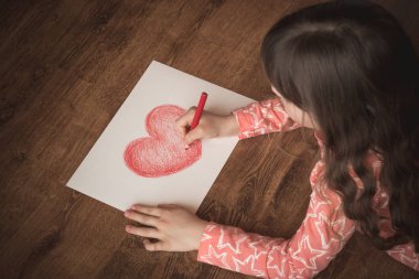 Küçük kız kırmızı pastel bir kalple çizer