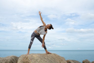 Kız taş yoga ile işgal, bir drenaj Asana, denizde güzel bir manzara bir midilli yogada