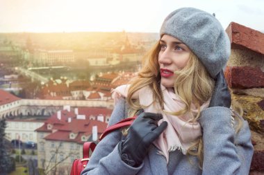Prag kadında. Czeh Cumhuriyeti. Kırmızı dudaklar ile gülümseyen güzel sarışın Bayan gri giyinmiş. City scape arka plan görünümü