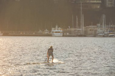 Günbatımında arka planda yatlarla gölde kürek çeken bir adam...