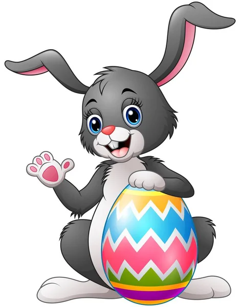 Bunny karikatura mávat rukou se drží velikonoční vajíčko — Stockový vektor