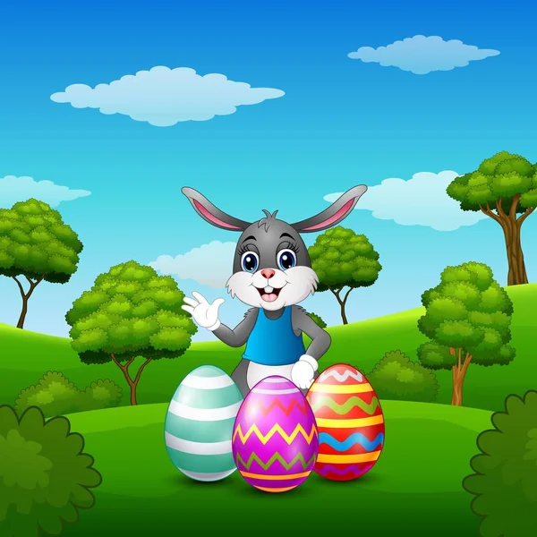 Cartoon coniglietto agitando mano con uova di Pasqua nel parco — Vettoriale Stock
