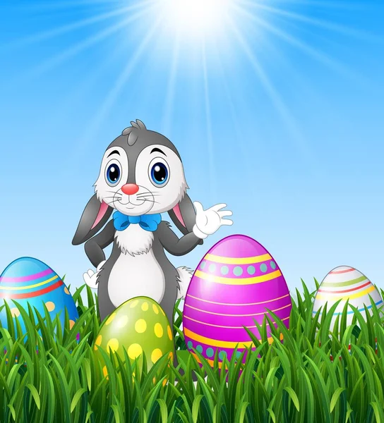 Conejo de Pascua de dibujos animados ondeando con huevos de Pascua en el fondo de la hierba — Vector de stock