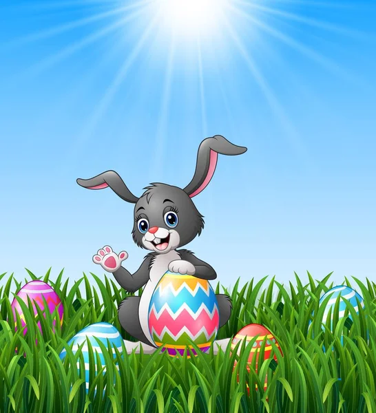 Conejito de dibujos animados agitando la mano con la celebración de huevo de Pascua en la hierba — Vector de stock