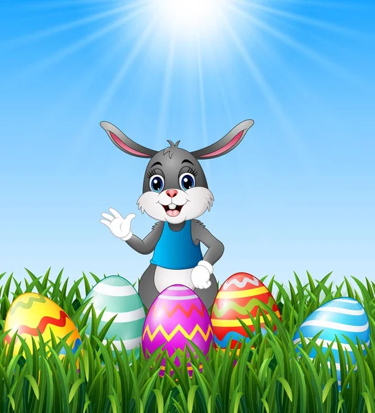 Conejito de dibujos animados agitando la mano con huevos de Pascua en la hierba — Vector de stock