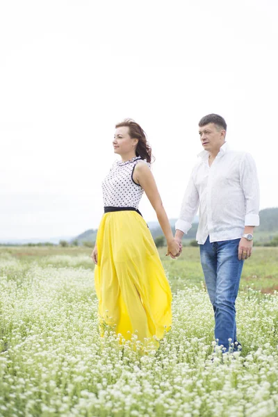 Amantes homem e mulher caminham no campo de flores . — Fotografia de Stock