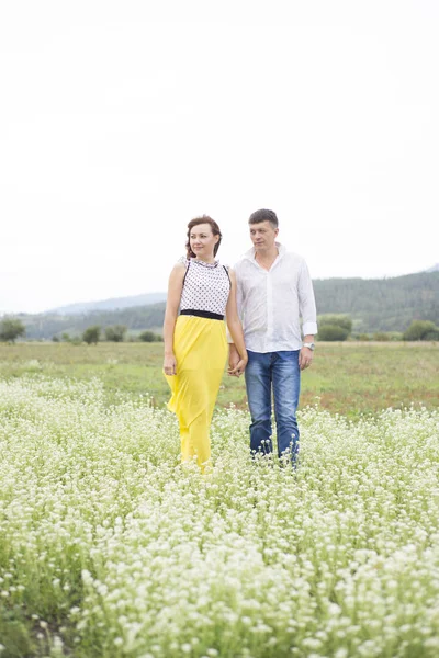 Amantes homem e mulher caminham no campo de flores . — Fotografia de Stock