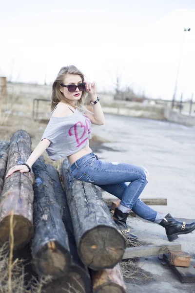Hermosa joven sentada en troncos en una zona industrial de th — Foto de Stock