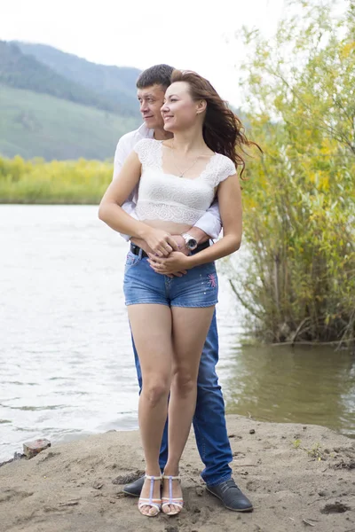 Amoureux homme et femme debout bras dans le bras au bord de la rivière . — Photo