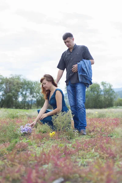 Älskare man och kvinna gå på fältet med röda blommor. — Stockfoto