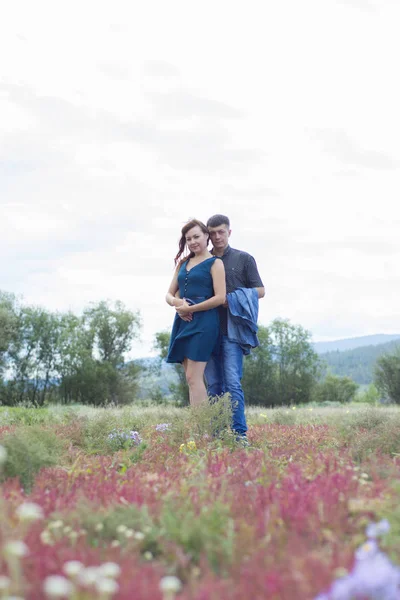 Amantes hombre y mujer caminan en el campo con flores rojas . —  Fotos de Stock