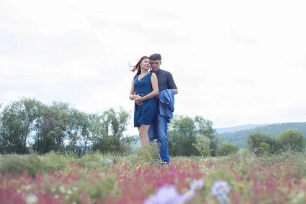 Amantes hombre y mujer caminan en el campo con flores rojas . — Foto de Stock