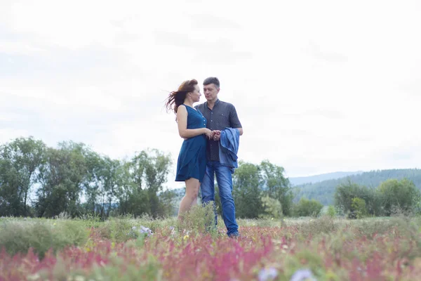 Milovníci muž a žena chodit na pole s červenými květy. — Stock fotografie
