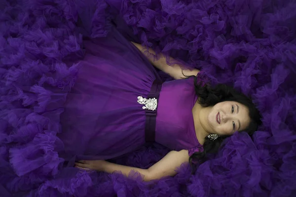 Full Asian woman lies in a lush lilac dress. — Stock Photo, Image