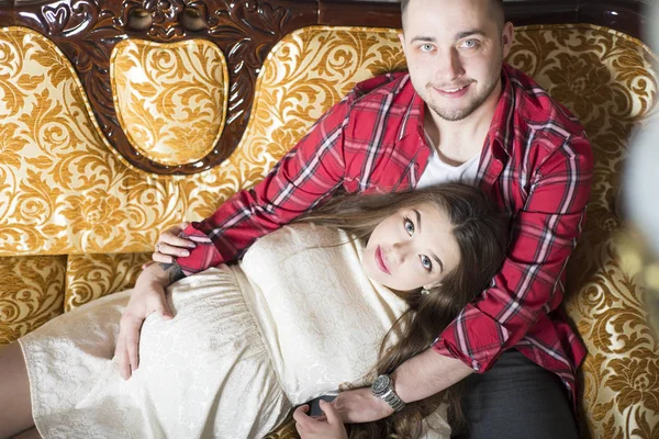 Молода вагітна жінка і її щасливий чоловік відпочивають на дивані — стокове фото