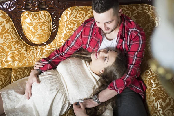 Eine junge schwangere Frau und ihr glücklicher Ehemann ruhen sich auf der Couch aus — Stockfoto