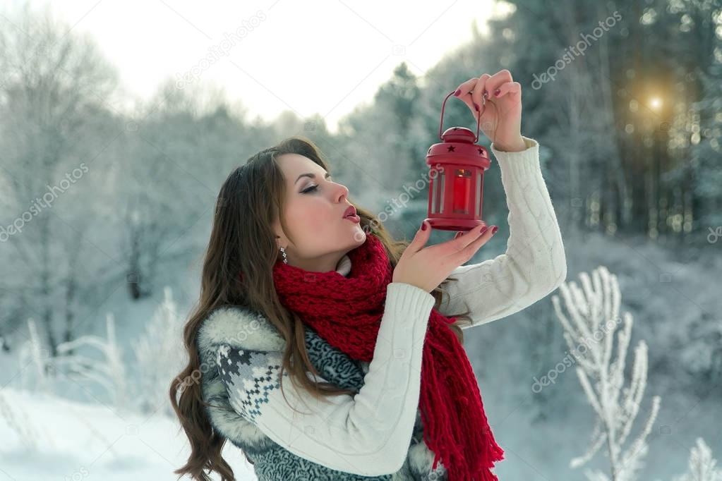 Beautiful young brunette woman in scarf holding red Christmas lantern with a candle