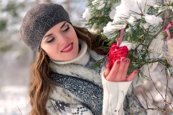 Χειμώνας εξωτερική πορτρέτο του ένα χαριτωμένο χαρούμενα θετική νεαρό κορίτσι με κόκκινη καρδιά διακόσμηση σε ένα φυσικό υπόβαθρο — Φωτογραφία Αρχείου