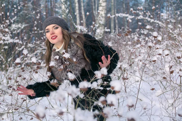 Piękna Brunetka Kobieta w beret i futro herb pozowanie i uśmiecha się na tle ośnieżonych lasów — Zdjęcie stockowe