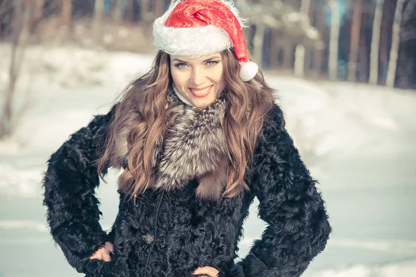 Femme de Noël dans le chapeau de Père Noël souriant sur un fond de forêt enneigée — Photo