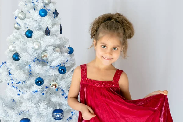 Bonne petite fille en robe de Noël. Bonne petite fille tenant jouet de Noël sur le sapin de Noël . — Photo