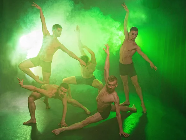 Група танцюристів молодих людей під час танців у студії на зеленому димчастому фоні — стокове фото