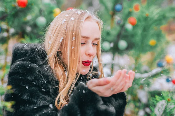 Joyeux jeune fille blonde dans une fourrure, soufflant de la neige par une journée enneigée sur le fond des arbres. L'effet de rétro, grain — Photo