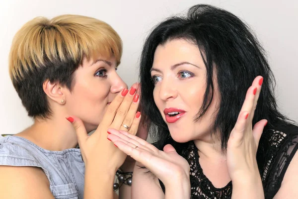 Portrait of a gossip girl telling a secret in the ear to her friend sitting on a couch at home — Stock Photo, Image