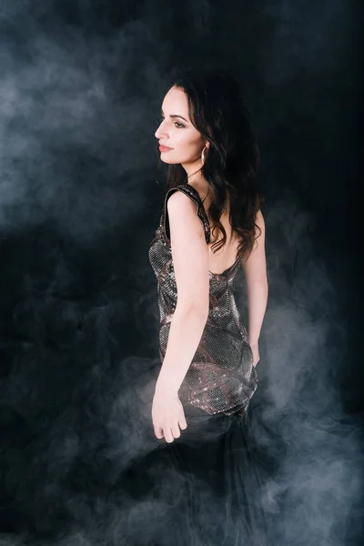 Όμορφη μελαχρινή γυναίκα σε ένα φόρεμα χορό και θέτοντας σε Studio σε σκούρο φόντο με καπνό — Φωτογραφία Αρχείου