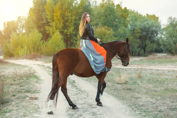 A beautiful girl is walking her horse. Focus on the girl. The warm tone of the image. Soft focus. — Stock Photo, Image
