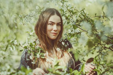 Mutlu gülümseyen genç kadın bahçede bahar çiçek zevk örme ceket