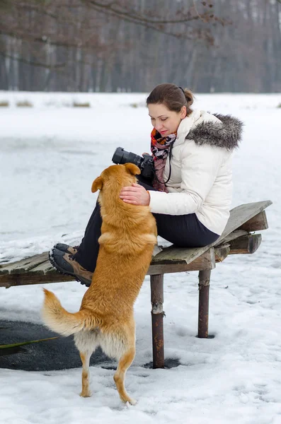 젊은 여자는 겨울에 그녀의 빨간 강아지를 쓰 다듬어 카메라와 재킷에. — 스톡 사진