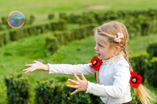 Menina bonita está brincando com bolhas em um parque . — Fotografia de Stock