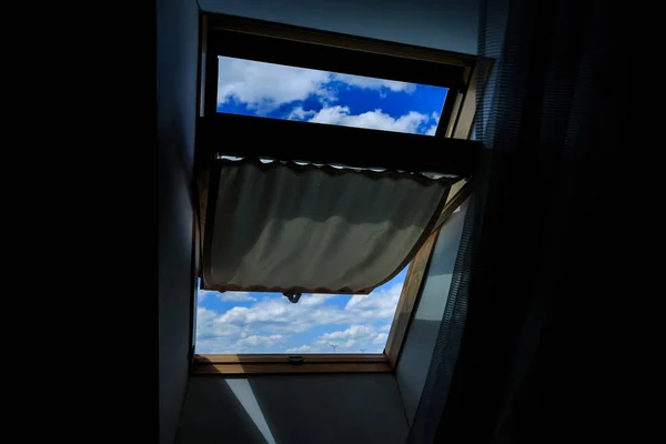 The window of the dark attic, open. A view of a clear blue sky with clouds. — Stock Photo, Image