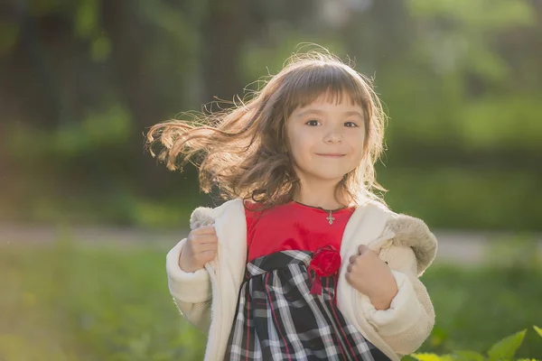 Menina bonita com cabelos longos em movimentos turbilhões e sorrisos, durante o pôr do sol no parque. O conceito de infância e liberdade . — Fotografia de Stock