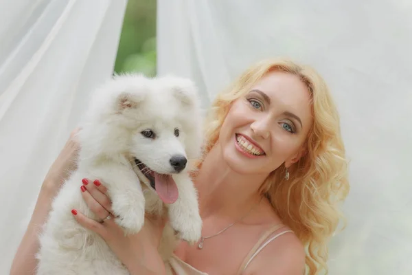 금발 여 자가 그녀의 팔에 흰색 강아지와 거리에 앉아 — 스톡 사진