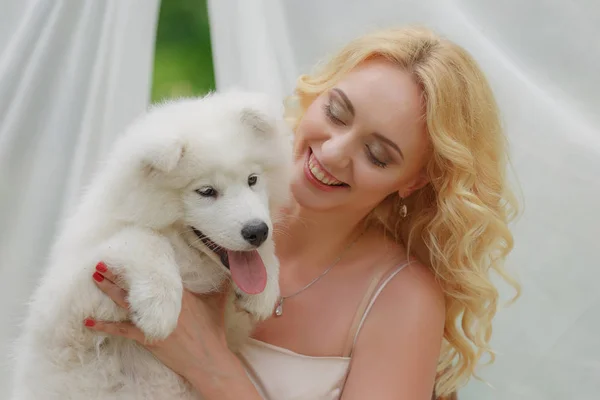 금발 여 자가 그녀의 팔에 흰색 강아지와 거리에 앉아 — 스톡 사진