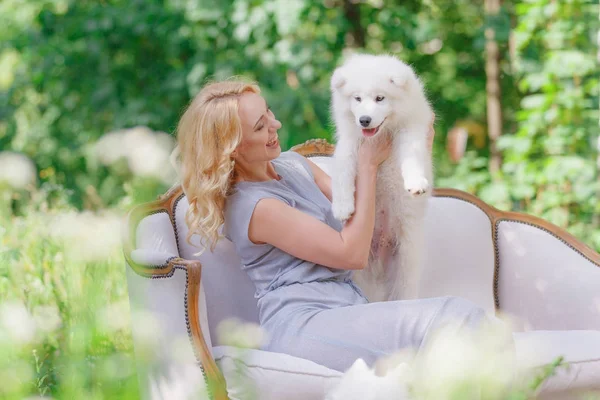 그녀의 팔에 여름 정원에서 복고풍 소파에 더 오래 된 흰 솜 털 개 흰색 강아지와 함께 아름 다운 소녀 — 스톡 사진