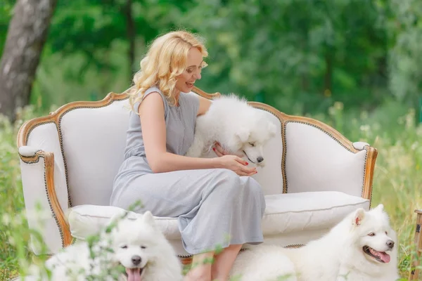 그녀의 팔에 여름 정원에서 복고풍 소파에 더 오래 된 흰 솜 털 개 흰색 강아지와 함께 아름 다운 소녀 — 스톡 사진